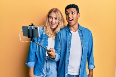 Genç, ırklar arası bir çift akıllı telefonuyla fotoğraf çekiyor. Çılgınlığı kutluyorlar ve başarıya hayret ediyorlar. Gözleri açık, heyecanlı çığlıklar atıyorlar.. 