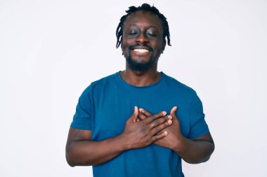 Saçları örgülü, elleri göğsünde, gözleri kapalı gülümseyen ve yüzünde minnet ifadesi olan Afro-Amerikan genç bir adam. sağlık kavramı. 