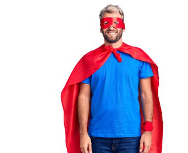 Yüzünde mutlu ve havalı bir gülümseme olan süper kahraman kıyafeti giyen genç sarışın adam. şanslı kişi. 