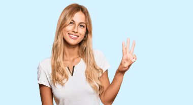 Güzel, sarışın, beyaz tişört giyen genç bir kadın üç numaralı parmaklarıyla onu gösterirken, kendinden emin ve mutlu gülümserken.. 