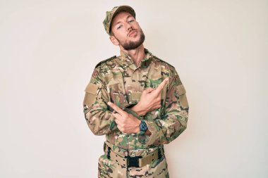 Kamuflaj üniforması giyen genç beyaz adam her iki tarafı da parmaklarıyla işaret ediyor, farklı yönlere. 