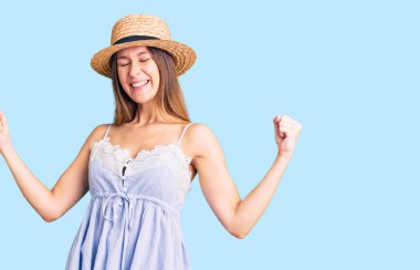 Güzel esmer, yaz şapkası takan çok mutlu ve heyecanlı genç bir kadın kolları havada, gülümseyen ve başarı için bağıran kazanan bir jest yapıyor. kutlama konsepti. 