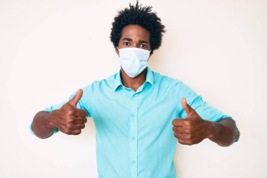 Afro saçlı, tıbbi maske takan yakışıklı Afro-Amerikan adam yüzünde ciddi bir ifadeyle rahatlamış. Basit ve doğal bir şekilde kameraya bakıyorsun.. 