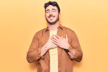 Gündelik kıyafetler giyen genç İspanyol adam elleri göğsünde, gözleri kapalı ve yüzünde minnet dolu bir jest ile gülümsüyor. sağlık kavramı. 