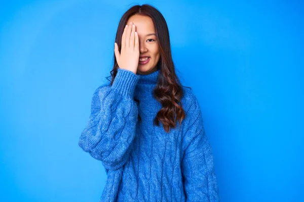 年轻美丽的中国姑娘 穿着宽松的冬季毛衣 一只手捂住一只眼睛 脸上挂着自信的微笑 感情令人惊讶 — 图库照片