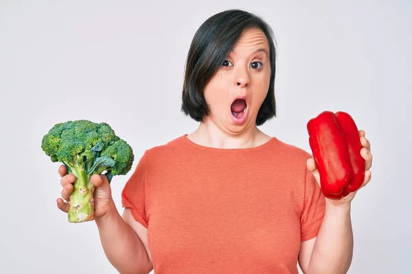 患有唐氏综合征的布鲁内特妇女提着花椰菜和红辣椒 害怕并震惊于惊讶而惊讶的表情 恐惧和兴奋的脸 — 图库照片