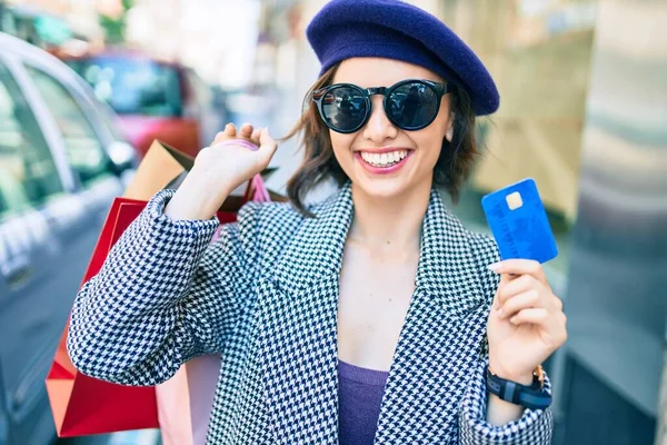Young beautiful girl smiling happy with french style holding shopping bags and credit card at street of city