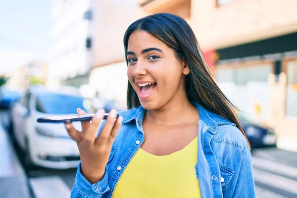 年轻的拉丁女人笑着高兴地在城市里用智能手机发送音频讯息 — 图库照片