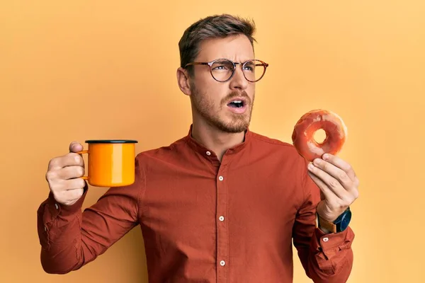 Hombre Caucásico Guapo Comiendo Donut Tomando Café Enojado Loco Gritando —  Fotos de Stock