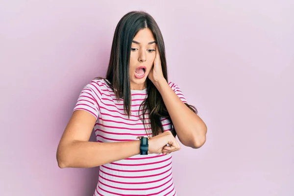 Młoda Brunetka Ubrana Luźne Ubrania Różowym Tle Patrząc Czas Zegarka — Zdjęcie stockowe