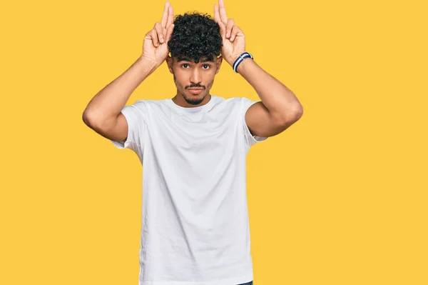 年轻的阿拉伯男子穿着随意的白色T恤 用手掌做着兔子耳朵的手势 看起来愤世嫉俗和怀疑 复活节兔子的概念 — 图库照片