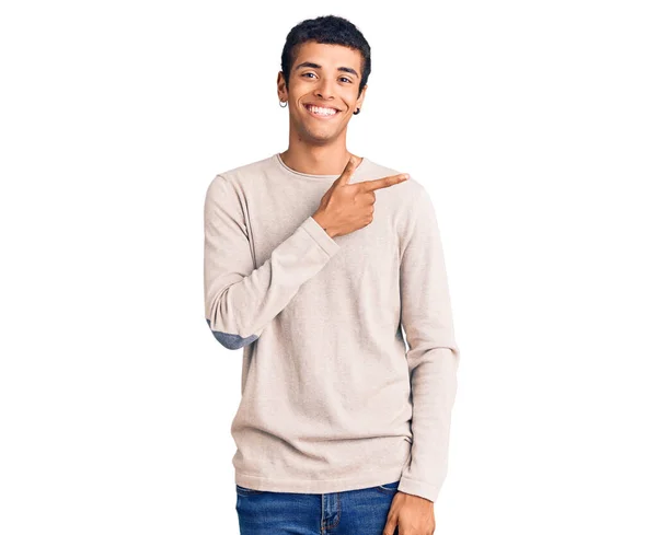 笑顔で陽気なカジュアルな服装をした若いアフリカ系アメリカ人男性が手と指で顔に幸せと自然な表情で側面まで指している — ストック写真