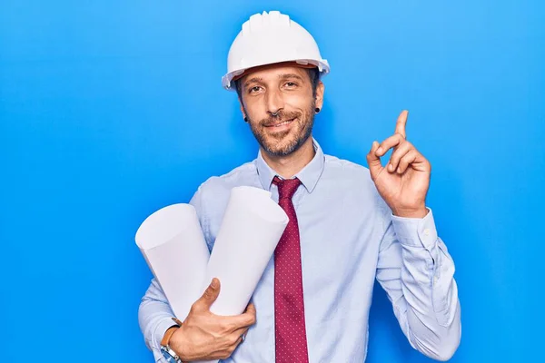 Joven Hombre Guapo Usando Arquitecto Hardhat Sosteniendo Planos Sorprendidos Con —  Fotos de Stock