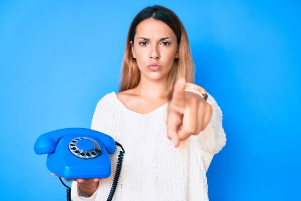 Young brunette woman using vintage telephone pointing with finger to the camera and to you, confident gesture looking serious