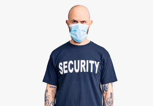 セキュリティTシャツを着た若いハンサムな男と顔に深刻な表情で医療マスク カメラを見ているだけで — ストック写真