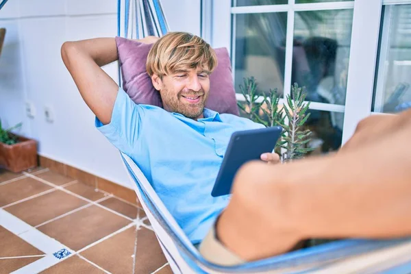 在他家阳台上的中年男子躺在一个装有触摸板装置的吊床上悠闲自在 — 图库照片