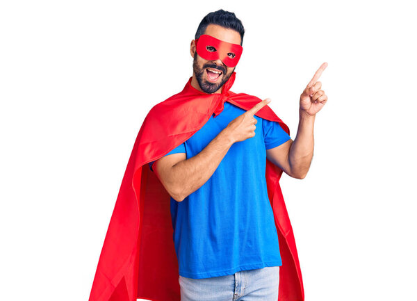 Young hispanic man wearing super hero costume smiling and looking at the camera pointing with two hands and fingers to the side. 