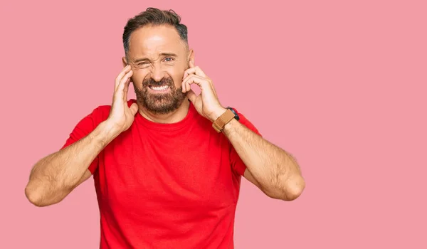 一个英俊的中年男人 穿着宽松的红色T恤 用手指捂住耳朵 对嘈杂的音乐感到恼怒 聋人概念 — 图库照片