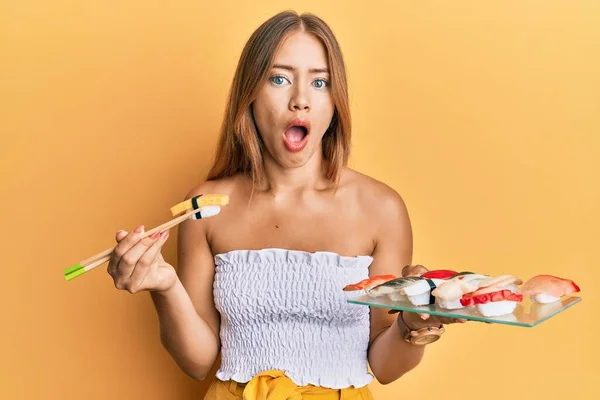 箸を使ってオムレツ寿司を食べる美しい若いブロンドの女性は恐れて 驚きと驚きの表情でショックを受けました 恐怖と興奮顔 — ストック写真