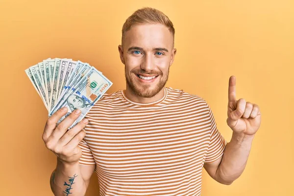 Young Caucasian Man Holding Dollars Smiling Idea Question Pointing Finger — Stock Photo, Image