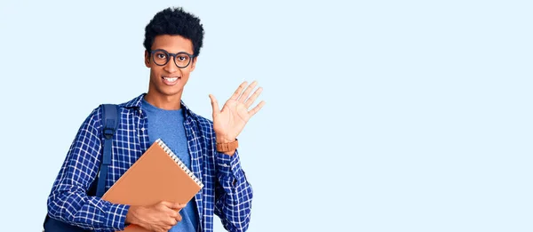 Young African American Man Wearing Student Backpack Holding Book Waiving — Stock Photo, Image