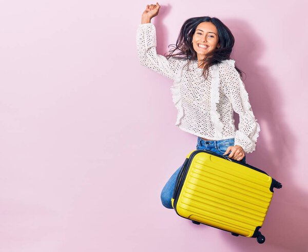 Young beautiful woman on vacation wearing summer clothes smiling happy. Jumping with smile on face holding cabin bag over isolated background