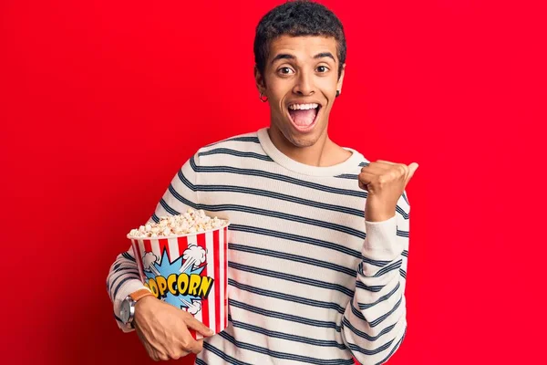 Young African Amercian Man Holding Popcorn Pointing Thumb Side Smiling — Stock Photo, Image