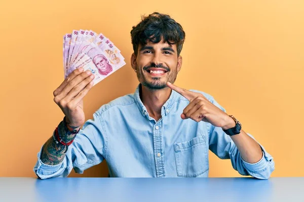 Jovem Hispânico Segurando Pesos Mexicanos Sentados Mesa Sorrindo Feliz Apontando — Fotografia de Stock