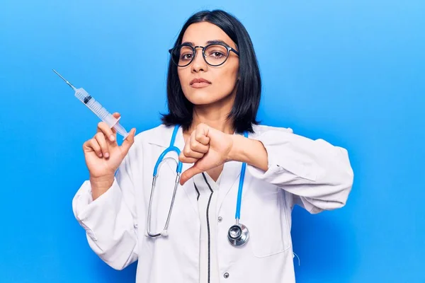 Young beautiful latin woman wearing doctor stethoscope holding syringe with angry face, negative sign showing dislike with thumbs down, rejection concept