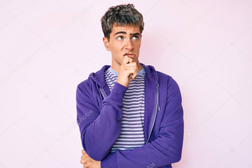 Young handsome man wearing casual purple sweatshirt serious face thinking about question with hand on chin, thoughtful about confusing idea 