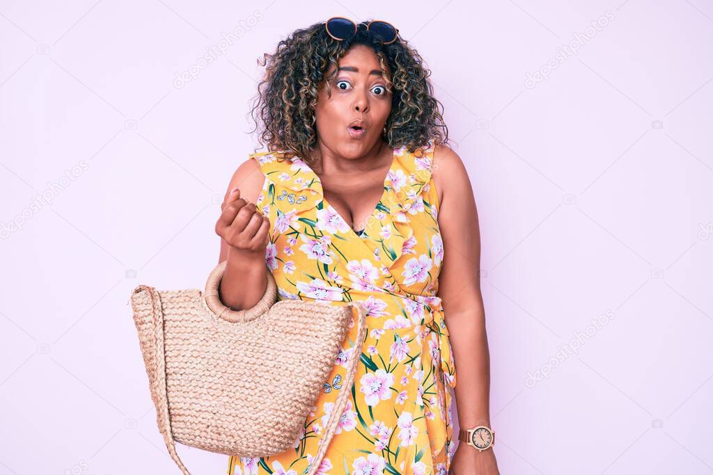 Young african american plus size woman wearing casual clothes holding summer wicker handbag scared and amazed with open mouth for surprise, disbelief face 