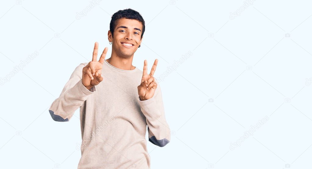 Young african amercian man wearing casual clothes smiling looking to the camera showing fingers doing victory sign. number two. 