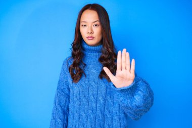 Kış süveteri giyen genç güzel Çinli kız avucunun içi gibi şarkı söylemeyi kesiyor. Yüzünde olumsuz ve ciddi bir jest olan uyarı ifadesi. 