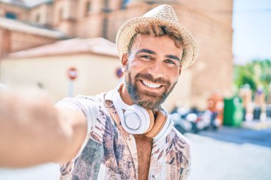 Tatilde olan genç İspanyol adam kulaklık takıyor ve şehrin caddesindeki kamerada selfie çekiyor.
