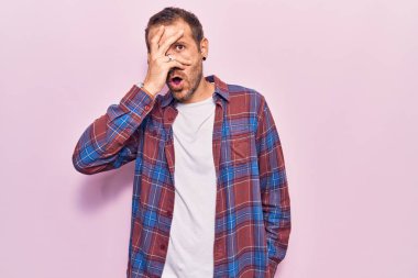 Gündelik kıyafetler giyen genç yakışıklı adam şok içinde yüzünü ve gözlerini eliyle kapatıyor, parmaklarından korkuyla bakıyor. 