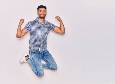 Genç, yakışıklı, sıradan kıyafetler giyen, mutlu gülümseyen bir İspanyol. Yüzünde tebessümle zıplıyor, beyaz arka planda yumruklar havada kutluyor.