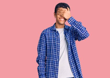 Gündelik giysiler giymiş genç Afro-Amerikan bir adam. Gülümsüyor ve elleri yüzüne gülüyor. Şaşırtmak için gözleri örtüyor. kör kavram. 