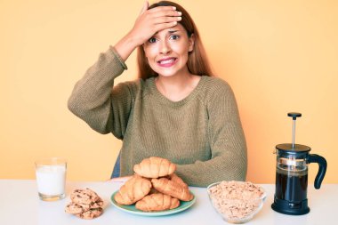 Genç esmer kadın masada oturmuş kahvaltı yapıyor. Stresli ve hayal kırıklığına uğramış, şaşırmış ve kızgın bir yüzü var. 
