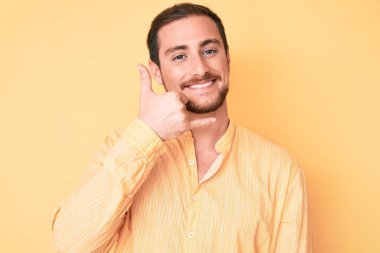 Genç, yakışıklı, sıradan kıyafetler giymiş, gülümseyen, el ve parmaklarıyla telefonla konuşan bir adam. iletişim kavramları. 