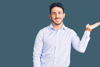 İş kıyafetleri giymiş, neşeli gülümseyen, eli avucunda kameraya bakan genç İspanyol bir adam.. 