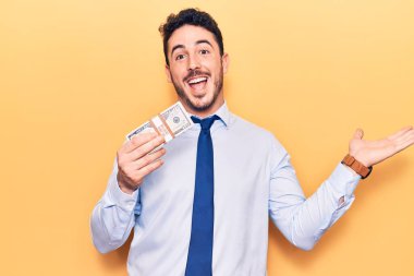 İş kıyafetleri içinde genç İspanyol bir adam dolar tutuyor başarıyı mutlu bir gülümsemeyle kutluyor ve kazanan el kaldırarak ifade ediyor 