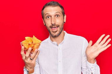 Patates cipsi tutan genç yakışıklı adam başarıyı mutlu bir gülümsemeyle kutluyor ve kazanan yüz ifadesini kaldırıyor. 