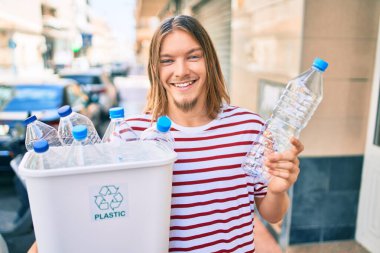 Sarışın, uzun saçlı ve sakallı beyaz bir adam plastik şişeleri geri dönüştürüyor.
