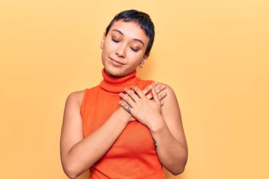 Elleri göğsünde gülümseyen sıradan kıyafetler giyen genç bir kadın. Minnettar bir yüz ifadesiyle gözleri kapalı. sağlık kavramı. 