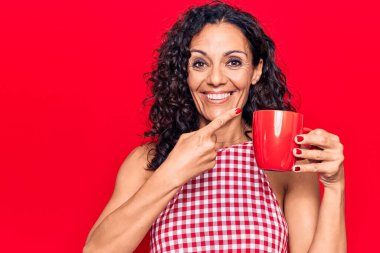 Orta yaşlı, güzel bir kadın, kahve fincanı içiyor, gülümsüyor, mutlu bir şekilde elini ve parmağını gösteriyor. 