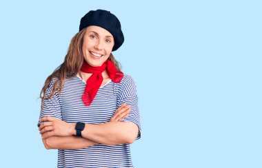 Fransız beresi ve çizgili tişört giyen, kollarını kavuşturup kameraya gülümseyen güzel sarışın kadın. pozitif kişi. 