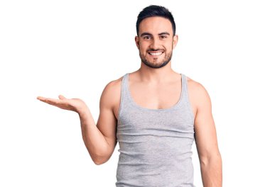 Mayo giyen, kolsuz tişörtlü, neşeli gülümseyen ve avuç içi kameraya bakan genç yakışıklı bir adam.. 