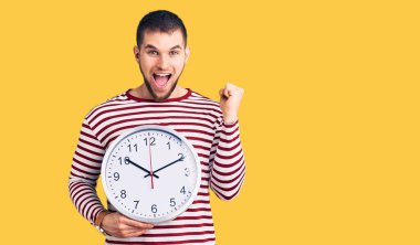 Büyük saat tutan genç yakışıklı adam gururla bağırıyor zaferi kutluyor ve başarıyı kollarını kaldırarak kutluyor. 