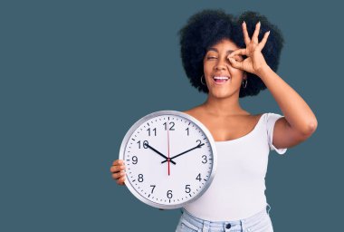 Büyük bir saat tutan Afrikalı Amerikalı genç kız gülümsüyor. Mutluluktan gülümsüyor. 