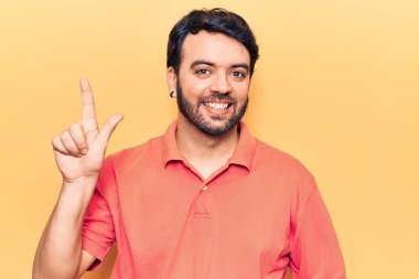 Bir fikir veya soruyla gülümseyen gündelik kıyafetler giyen genç İspanyol adam, bir numara, mutlu bir yüzle işaret ediyor. 